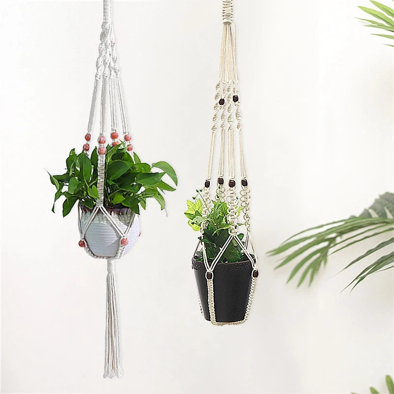 Macrame plant hanger with a potted green plant hanging from a macrame cord on a white wall.