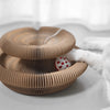 A close-up of a brown foldable accordion cat scratcher with a white catnip ball being held by a paw.