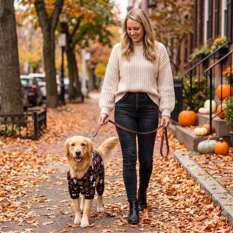 A woman is walking a golden retriever through a path covered in autumn leaves.