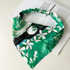 Diadema o pañuelo elástico floral verde y blanco mostrado sobre un fondo blanco.