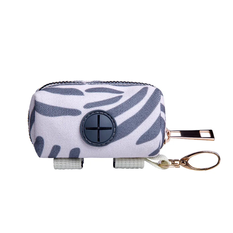 Dispenser para bolsas de excremento de mascota con cremallera, estampado de cebra blanco y gris y enganche de correa dorado.