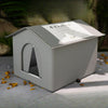 A light gray, foldable pet bed with a pitched roof and an arched entrance is shown on a surface.