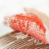 A hand gently rubs an orange-tipped rubber pet grooming brush onto a wooden surface to create instant rich foam.