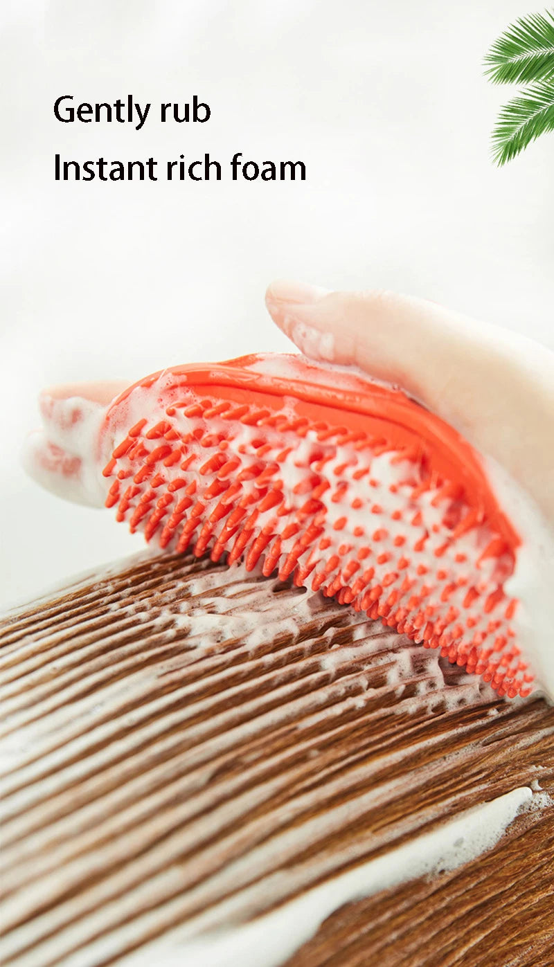 A hand gently rubs an orange-tipped rubber pet grooming brush onto a wooden surface to create instant rich foam.