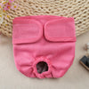 A pink reusable dog diaper with a cutout for the abdomen is displayed on a woven mat.