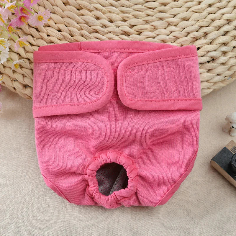 A pink reusable dog diaper with a cutout for the abdomen is displayed on a woven mat.
