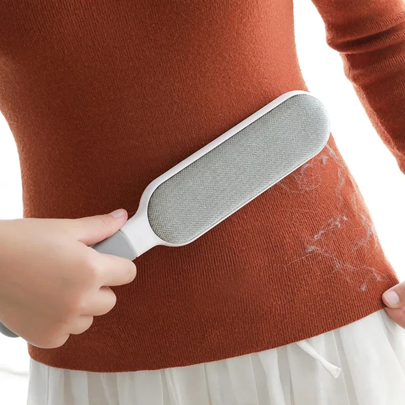 A hand holds a gray reusable lint remover brush against a reddish-brown garment.