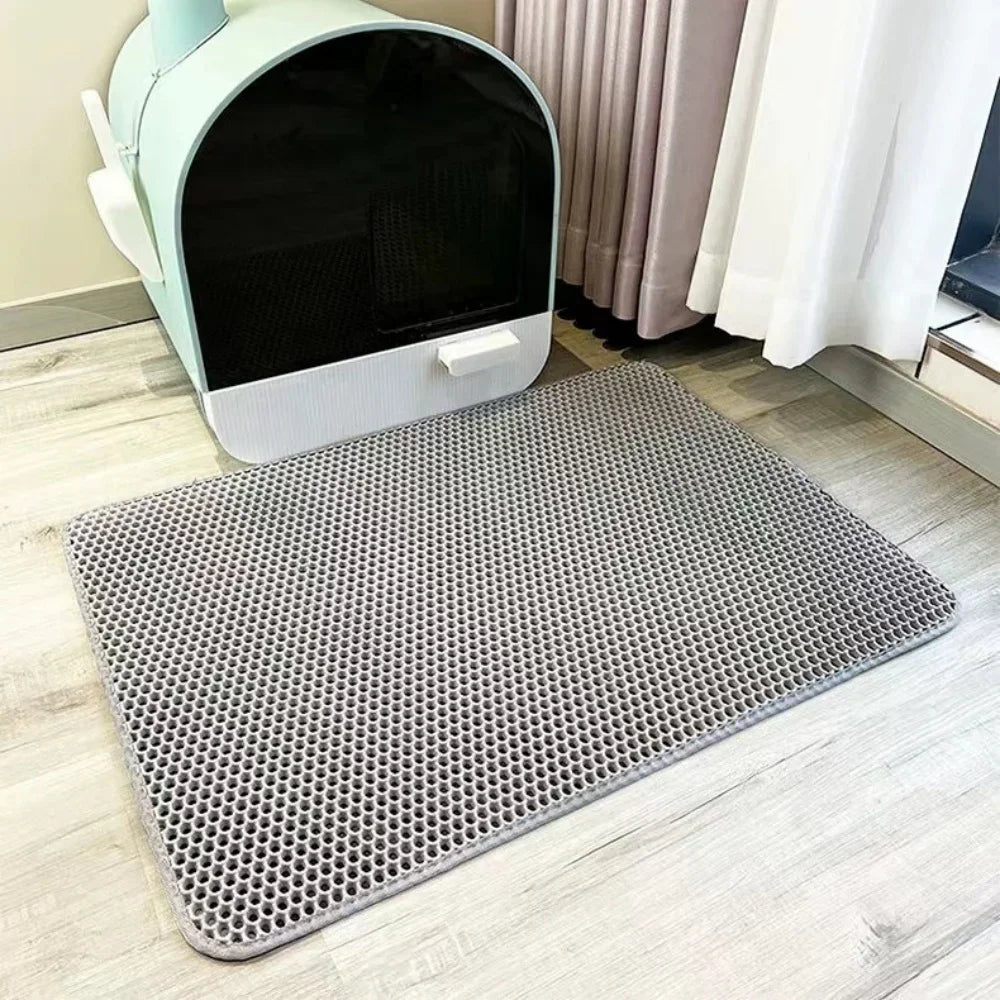 A gray waterproof cat litter mat with a non-slip base is shown on a light wooden floor.