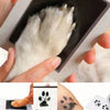 A hand holds a white paw print made of ink on a card, demonstrating an inkless pet paw print kit.