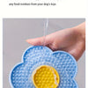 A hand is washing a blue silicone flower-shaped mat under running water to clean food residues from dog toys.