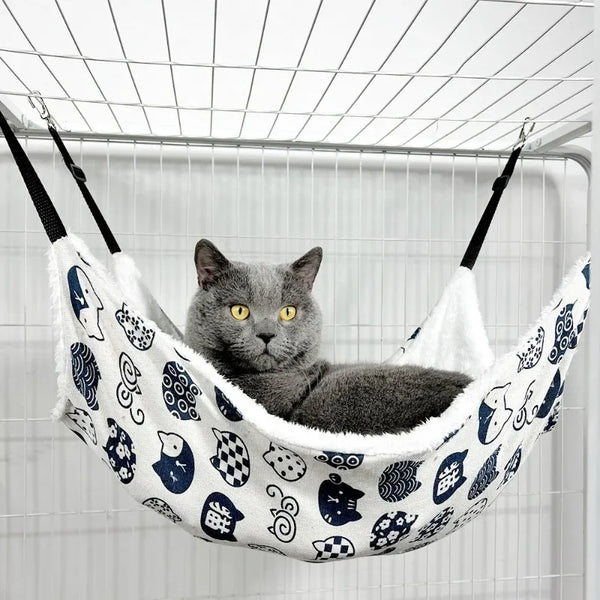 A gray cat is relaxing in a white and blue patterned hanging hammock for sleeping.