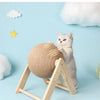 A fluffy gray cat is playing with a round sisal rope ball toy supported by a wooden base.