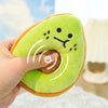 A hand is holding a bright green avocado plush toy with a smiling face and orange skin.