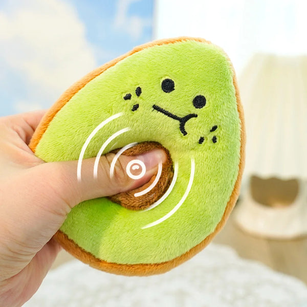 A hand is holding a bright green avocado plush toy with a smiling face and orange skin.