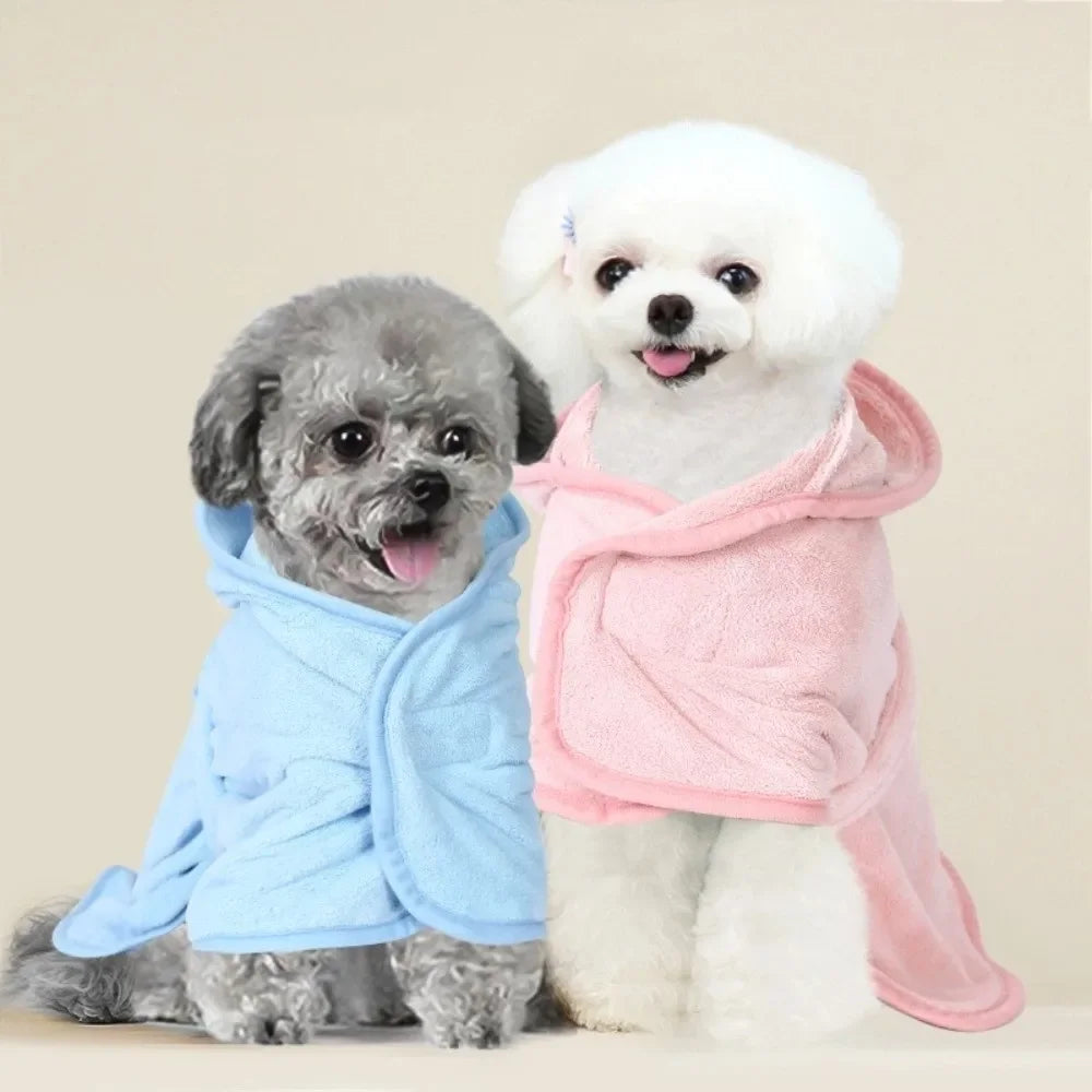 A fluffy white dog wearing a pink pet bath robe stands next to a grey dog wearing a blue pet bath robe.