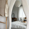A white and striped pet dress is displayed on a wooden hanger next to a woven bag in a bright room.