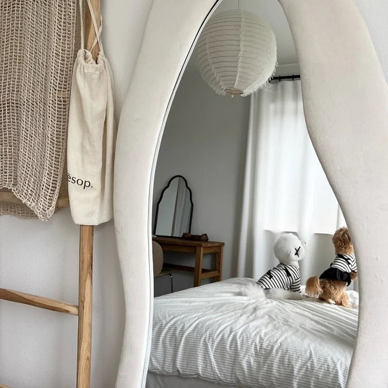 A white and striped pet dress is displayed on a wooden hanger next to a woven bag in a bright room.