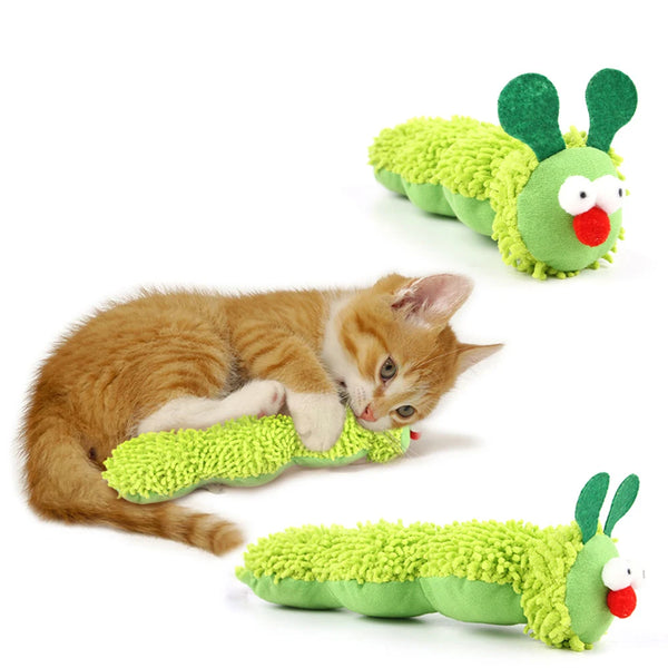 A small orange kitten is lying next to a green, fuzzy cat chew toy with green ears and a red nose.
