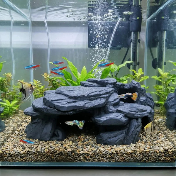 A realistic 3D printed fish tank rockery ornament featuring dark rocks and green plants with small colorful fish.