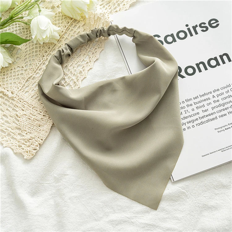 A soft sage green bohemian paisley triangle head scarf laid on a white textured fabric.