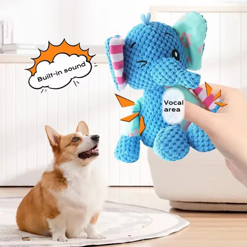 A hand holds a blue plush elephant toy with a vocal area, next to a small dog.