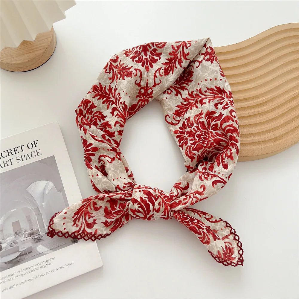 Foulard en coton floral rouge et blanc noué en nœud, posé sur un objet en bois clair.