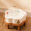White ceramic slow feeder cat bowl with a decorative tree design resting on a natural wooden stand.