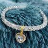 A sparkling crystal heart pendant on a silver collar against a blue faux fur background.