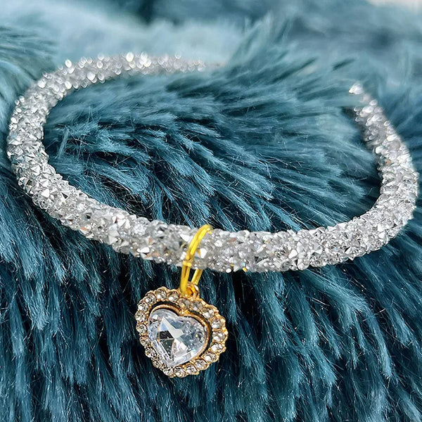 A sparkling crystal heart pendant on a silver collar against a blue faux fur background.