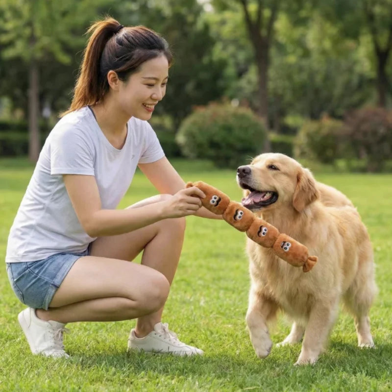 A woman is playing with a dog, offering it a durable plush squeaky sausage chew toy in a grassy outdoor setting.