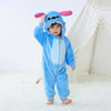 A baby wearing a blue cartoon animal hooded romper with pink ears standing in front of a white tent.