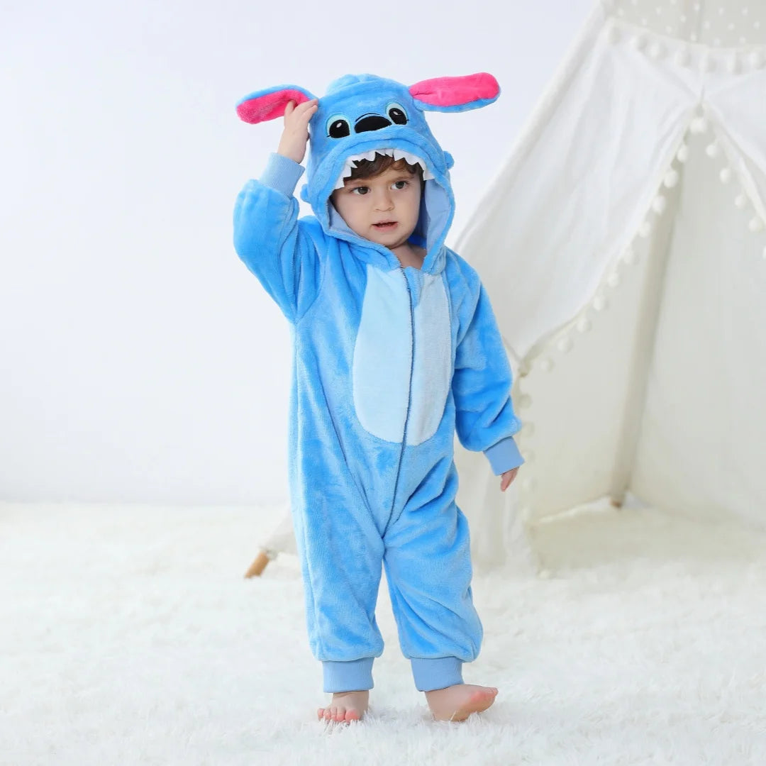 A baby wearing a blue cartoon animal hooded romper with pink ears standing in front of a white tent.