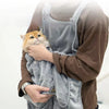 Una persona sostiene un gato naranja peludo dentro de un petcarrier gris para exteriores.
