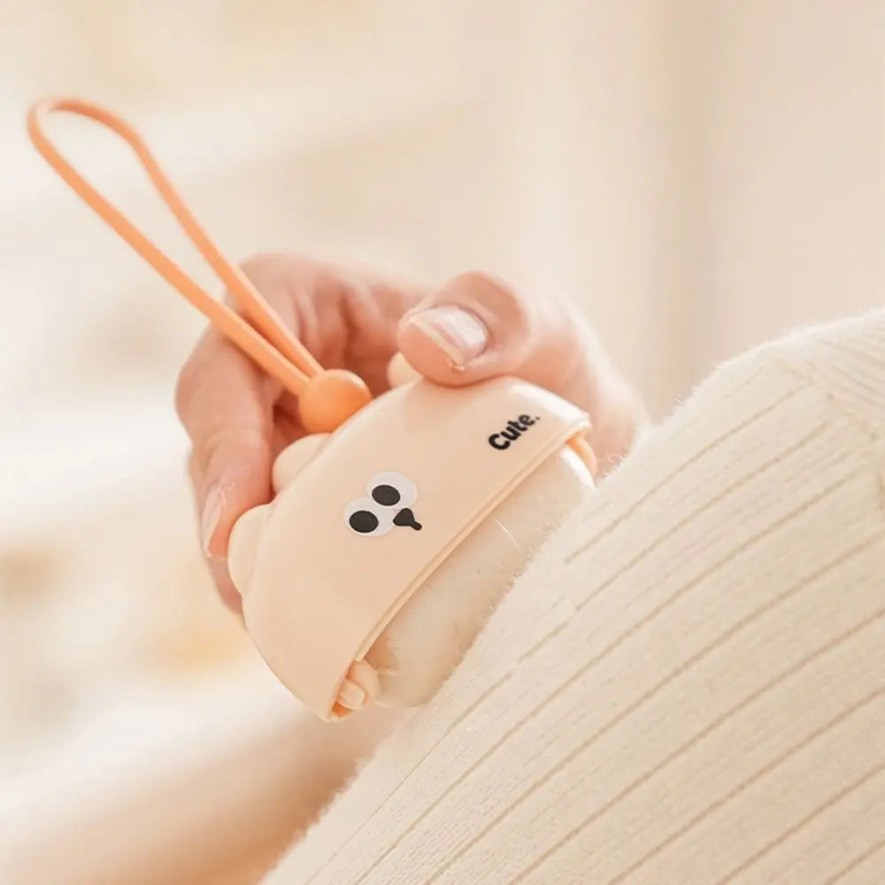 A hand holds a beige reusable pet hair roller with a cute cartoon design and an orange loop.