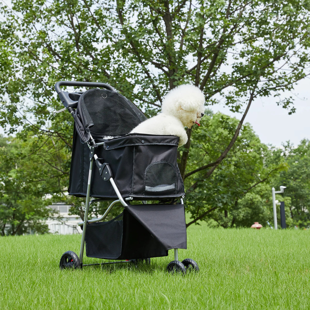 A black 3-wheel foldable pet stroller with a white, fluffy dog is shown outdoors in a grassy field.