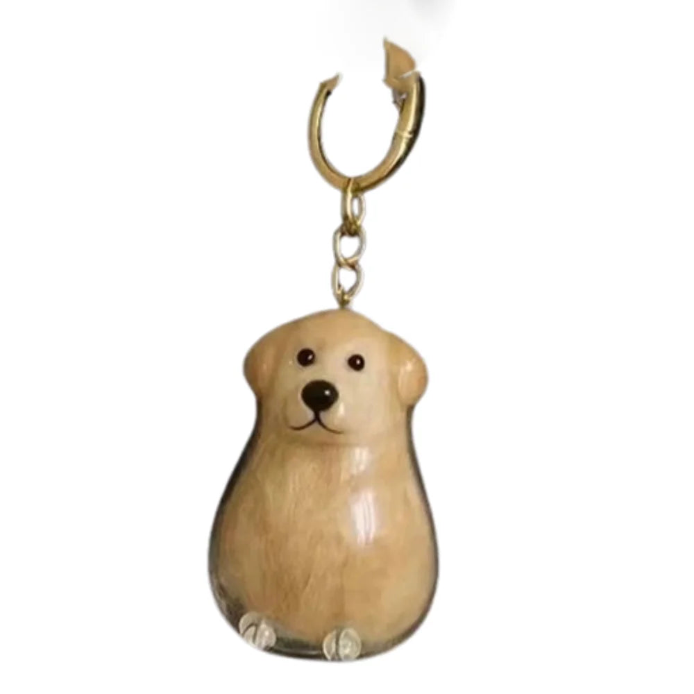 Un pequeño dije de perro de color marrón claro sujeto a un anillo de llavero de color dorado.