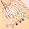 Une chaîne de perles de nacre avec des pendentifs de gemmes colorées est présentée sur une surface en bois.