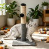 A gray cat sits in front of a cylindrical sisal scratching post with a fuzzy top and a gray base.