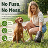 A woman is kneeling on grass with a dog and a package of dog waste bags for cleanup.