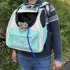 Eine Person trägt einen hellgrünen zusammenklappbaren Hundetransporte-Rucksack mit schwarzer Futter und einer türkisen Tasche