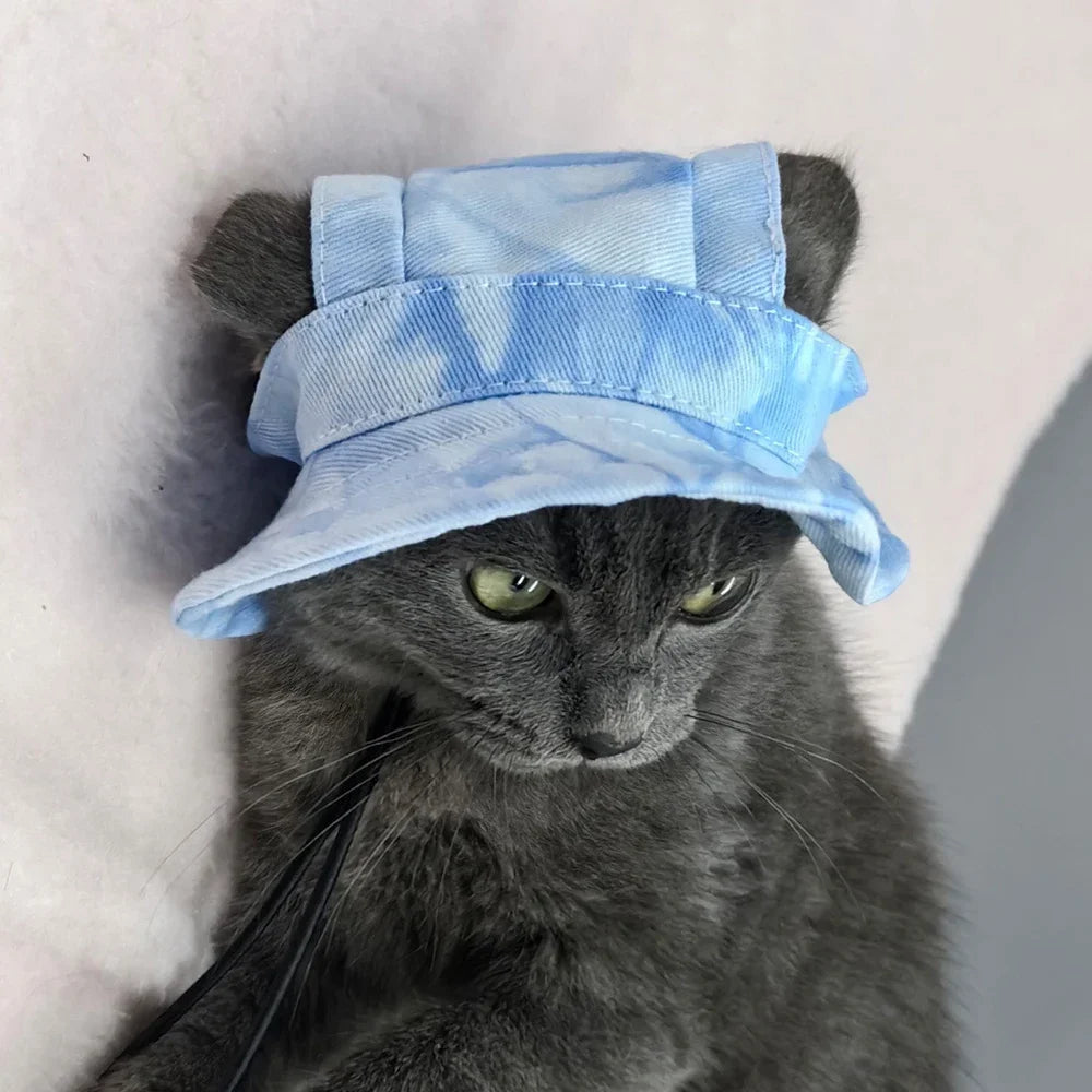 Un gato gris usando un sombrero de sol azul claro y rayado con orificios para las orejas.