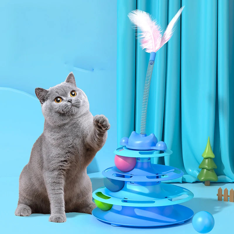 A gray cat sits next to an interactive toy tower featuring multiple rotating platforms and a feather ball.