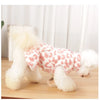 A fluffy white dog wearing a leopard print princess dress standing on a wooden surface.