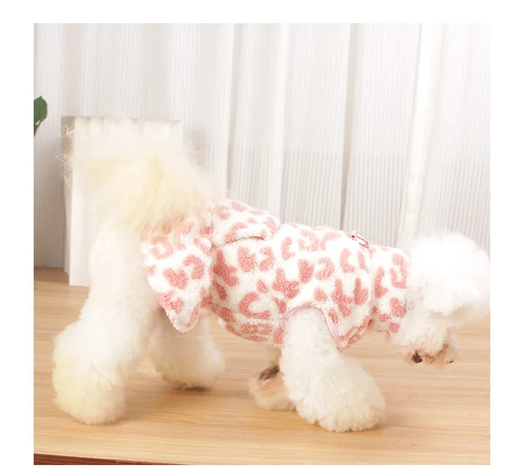 A fluffy white dog wearing a leopard print princess dress standing on a wooden surface.