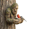 A resin sculpture of a tree hugger with a bird feeder perched on his hand.