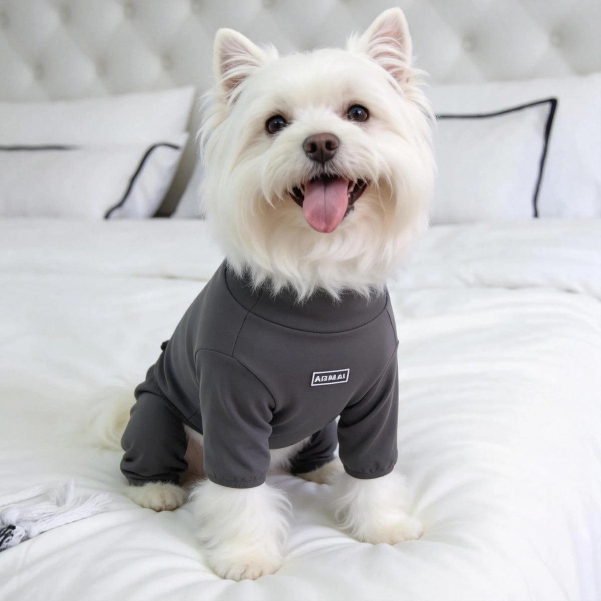 A white dog wearing a gray cozy pajama top with a high collar lying on white bedding.
