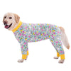 A golden retriever wearing a light-colored jumpsuit with a colorful cartoon animal print.
