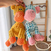 A hand is holding a yellow and orange squeaky donkey plush toy for dogs.