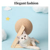 A white cat is relaxing on a wooden base next to a large, round beige sisal rope ball toy.