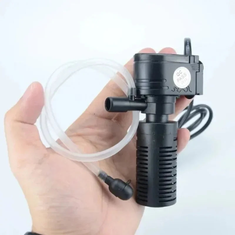 A hand holds a black 3-in-1 aquarium filter pump with tubing and a power cord.